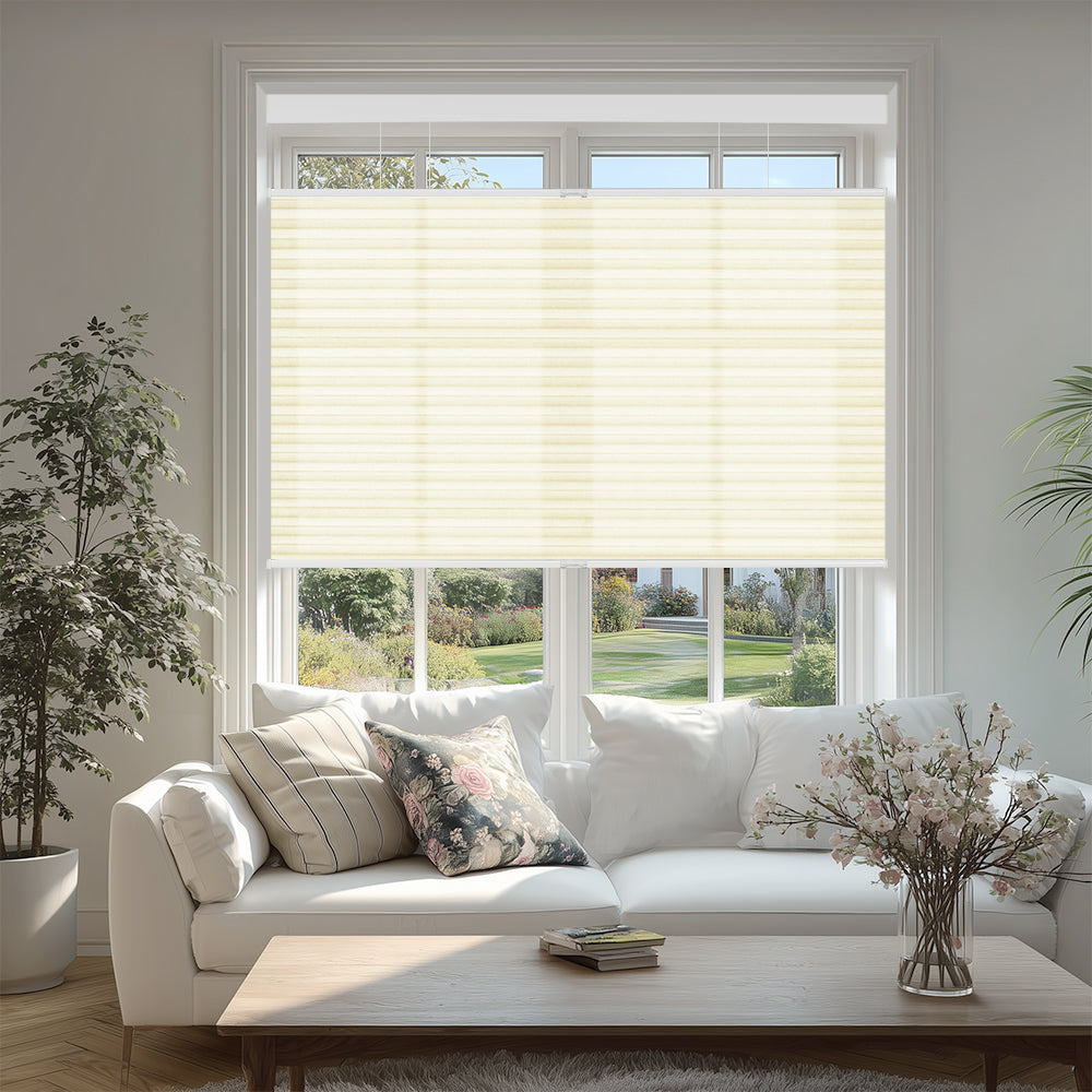 Bright living room with white sofa, floral and striped cushions, beige window blinds, and potted plants