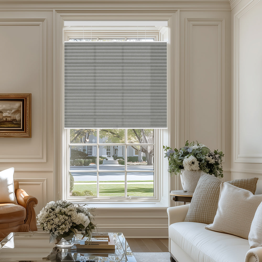 Elegant living room with gray cellular window shade, white sofa, leather chair, and floral arrangements