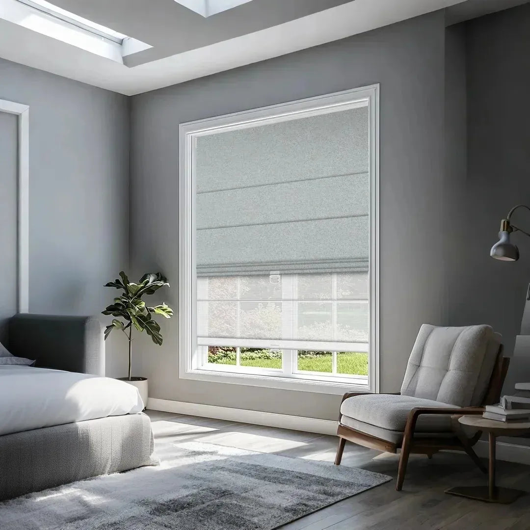 Modern bedroom with gray roman shades on large window, gray upholstered bed, armchair, and potted plant