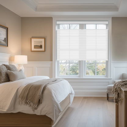 Cozy bedroom with white bedding, beige throw, wood furniture, table lamp, and large window with white blinds