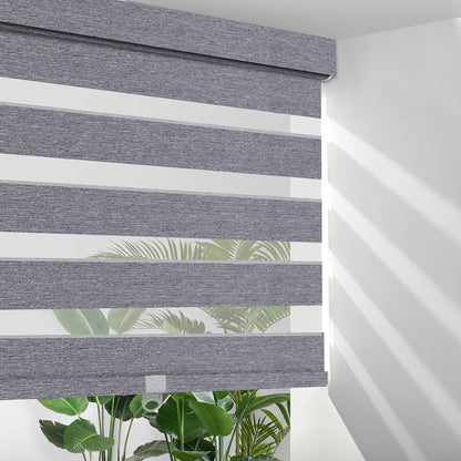 Grey fabric zebra blinds partially open with sunlight and green indoor plants behind