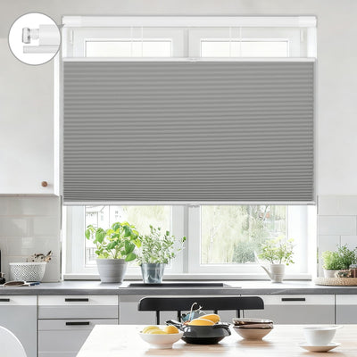 Modern kitchen window with gray cellular shades, countertop plants, and tableware in bright setting