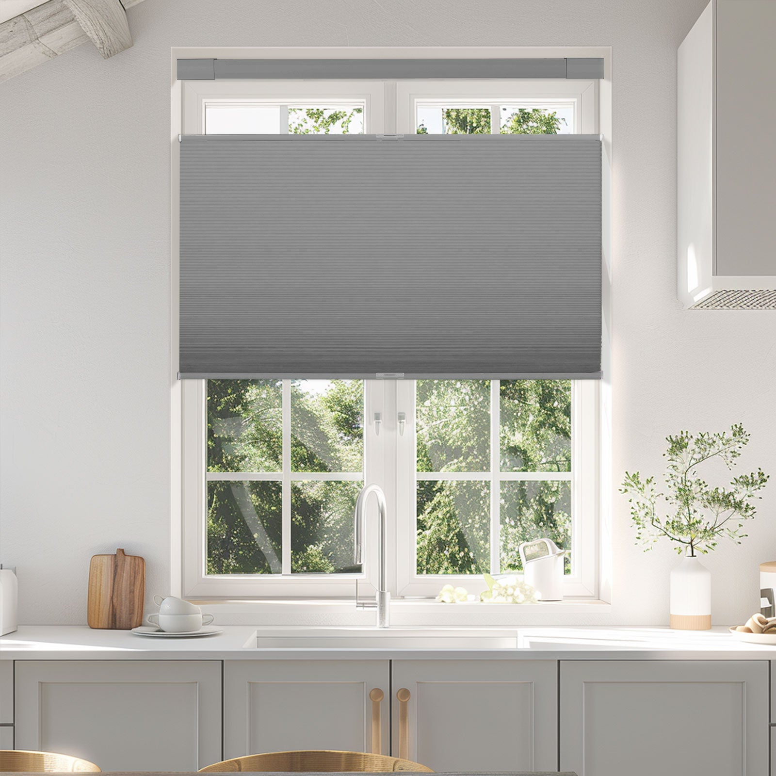 Modern kitchen window with gray cellular shades partially closed, white cabinets and faucet