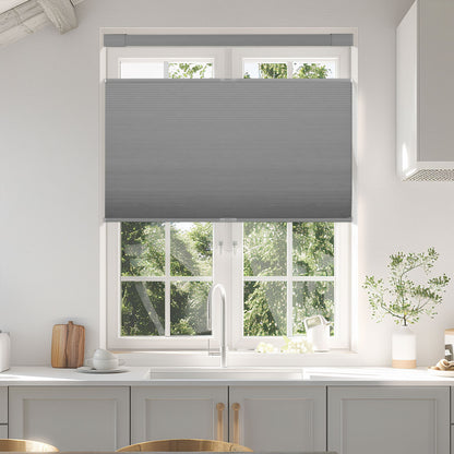 Modern kitchen window with gray cellular shades partially closed, white cabinets and faucet