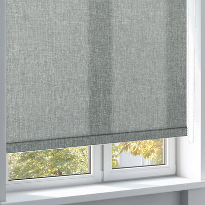 Modern grey textured roller blind partially covering white window with autumn foliage outside